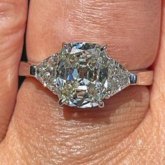 a woman's hand holding a three stone ring with an oval shaped diamond in the center