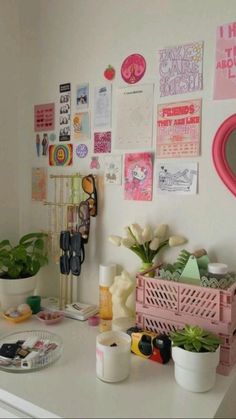 a white desk topped with lots of clutter and flowers next to a wall covered in pictures