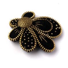 a black and gold flower brooch with beaded details on the center, sitting on a white surface