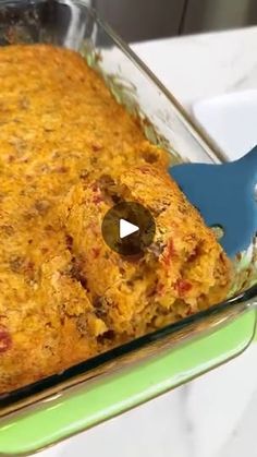 a glass casserole dish filled with food and a blue spatula in it