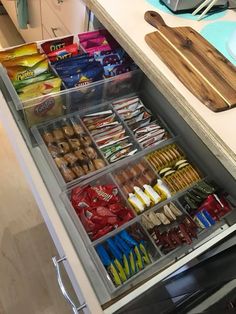 an organized kitchen drawer filled with snacks and other food items on a counter top next to a cutting board