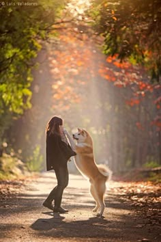 a woman standing next to a brown and white dog on top of a dirt road