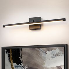 a painting is hanging on the wall next to a light fixture that has been turned on