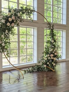 a wedding arch with flowers and greenery on the floor in front of two windows