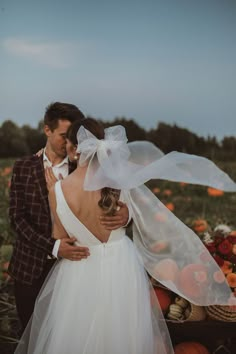 a bride and groom standing in the middle of a field with pumpkins behind them