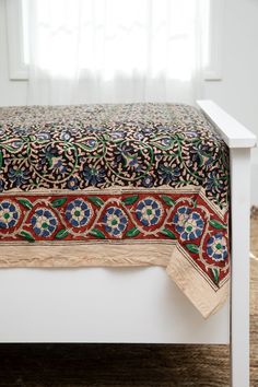 a white bed topped with a colorful bedspread covered in an intricately designed blanket