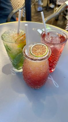 three glasses filled with different types of drinks sitting on a white table top next to each other