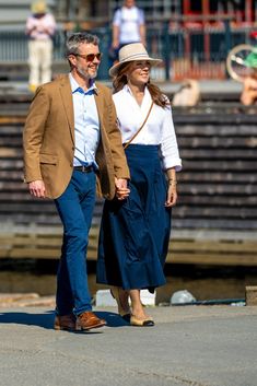 the man and woman are walking together down the street in their dressy clothes, hats, and sunglasses