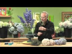 a man standing in front of a table with flowers and plants on top of it