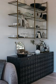 a living room filled with furniture next to a wall mounted shelf full of bottles and glasses