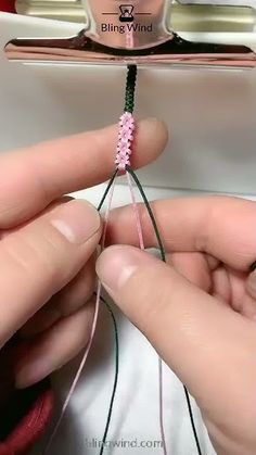 someone is working on the end of a piece of string with pink and green beads