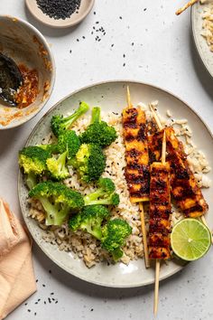 chicken and broccoli skewers with rice on a plate next to other dishes