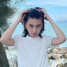 a young woman holding her hair in front of the ocean