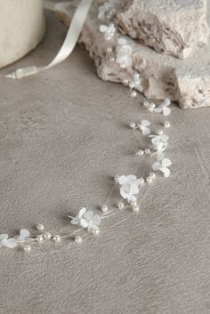 a white necklace with flowers and pearls on top of a stone wall next to rocks