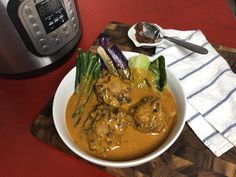 a white bowl filled with meat and vegetables next to an instant pressure cooker on a red table