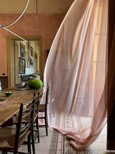 a dining room table with chairs and a sheer curtain hanging from the ceiling over it