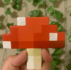 a hand holding up a piece of paper that looks like a mushroom with red and white squares on it