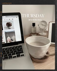 an open laptop computer sitting on top of a wooden table next to a bowl and clock