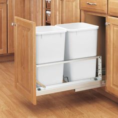 an open cabinet in a kitchen with wooden floors and cabinets on either side, there is a white drawer that has two plastic bins under it