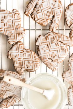 some heart shaped cookies on a cooling rack next to a bowl of milk and a wooden spoon