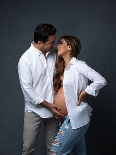 a man and woman standing next to each other in front of a dark background with their hands on the stomach