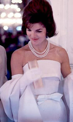 a man standing next to a woman in a white dress and pearls on her necklace