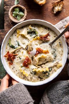 a bowl of pasta with spinach and tomato sauce on a wooden table next to bread