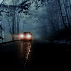 a car driving down the road at night in the foggy forest with its headlights on