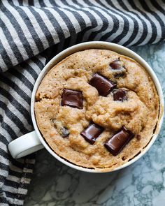 a chocolate chip cookie in a white mug on a black and white striped towel next to a cup of coffee