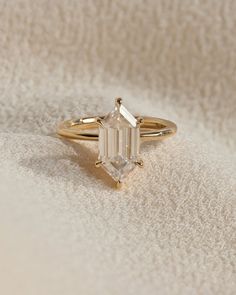 a gold ring with an emerald cut diamond in the center on a white cloth background