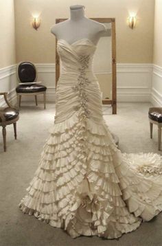 a wedding dress on display in a room with chairs and a mirror behind it that has been made out of ruffled fabric