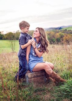 a woman sitting on top of a wooden crate next to a boy in a field