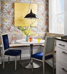 a table with two chairs and a vase on it in front of a wallpapered window