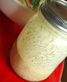 a mason jar filled with dressing sitting on top of a red cutting board next to a bowl of salad