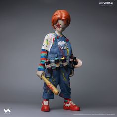 a creepy doll holding a baseball bat and wearing overalls with paint splattered on it