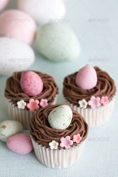 three cupcakes sitting on top of each other in front of some white and pink eggs