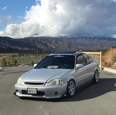 a silver car parked in a parking lot with mountains in the background