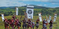 a group of toy figurines holding flags and swords in front of a grassy field