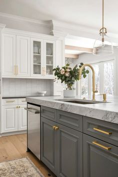 a kitchen with white cabinets and marble counter tops, gold pulls on the faucet