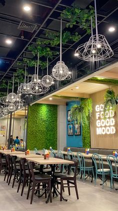 an indoor restaurant with tables and chairs, hanging plants on the wall above them that read get good mood