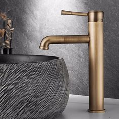 a bathroom sink with a gold faucet next to a black bowl filled with flowers