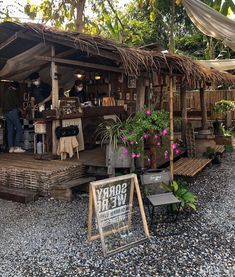 a small wooden building with plants and people standing outside on the front porch, surrounded by gravel