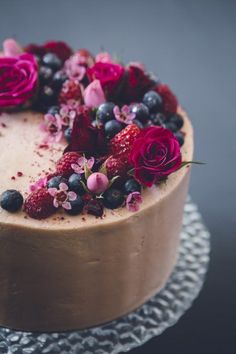 a cake with chocolate frosting and fresh berries on top is decorated with pink flowers