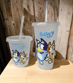 two plastic cups sitting on top of a wooden table next to each other with cartoon characters painted on them