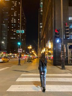 a woman walking across a cross walk at night