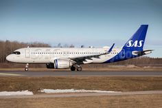 a white and blue jet airliner on runway with trees in the backgroud