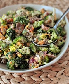 a white bowl filled with broccoli and other food on top of a woven place mat