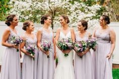 a group of women standing next to each other in front of white flowers and trees