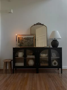 a black cabinet with glass doors in a living room next to a lamp and mirror