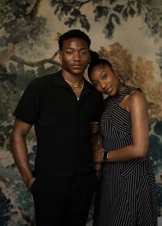 a man and woman standing next to each other in front of a floral wallpaper